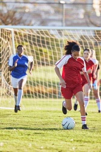 Sports team, girl soccer and kick ball on field in a tournament. Football, competition and athletic female teen group play game on grass. Fit adolescents compete to win match at school championship