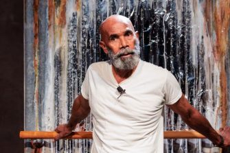 An older Aboriginal man with a grey beard performs onstage