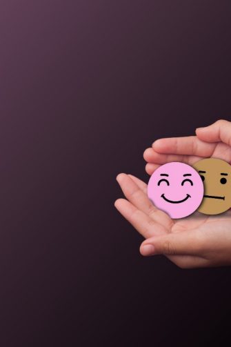 Hands holding three emotion face symbols sad, neutral, and happy on dark background representing mental health awareness, mood change, emotional balance, and psychological wellbeing,