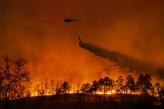 Fire fighting helicopter dropping water over bushfire
