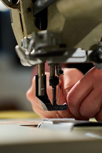 Close-up of hands threading a heavy-duty industrial sewing machine in a workshop