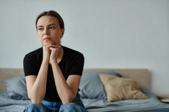 Middle-aged woman sitting on bed, deep in thought, hand on chin.