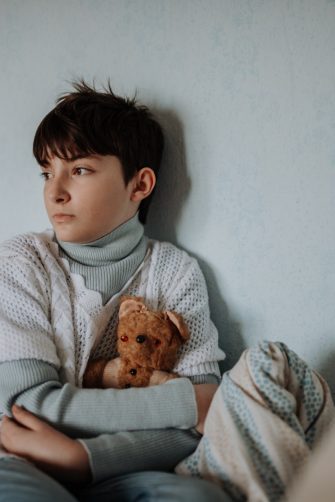 Poor young girl in bedroom holding her old teddy bear