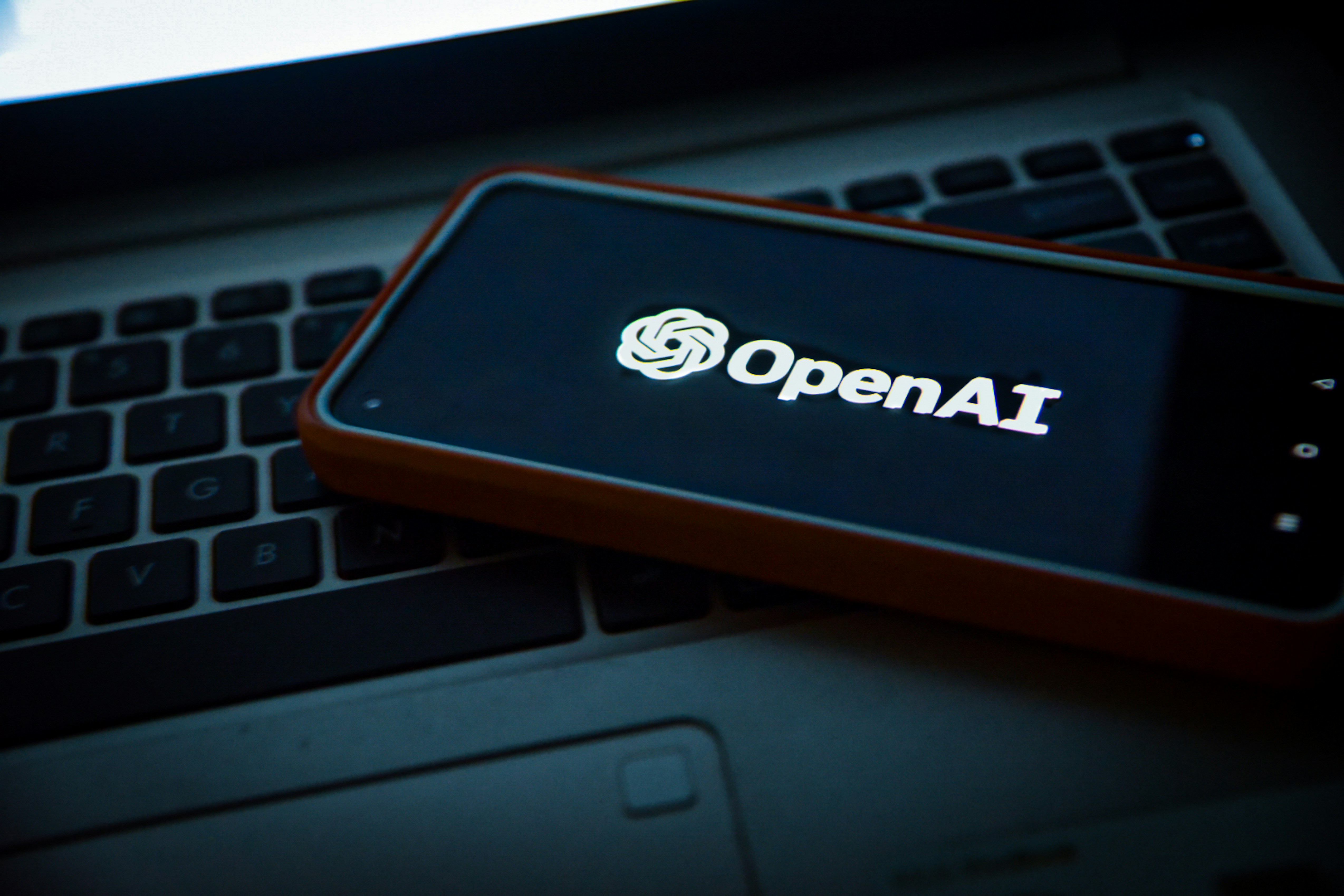 OpenAI logo on a mobile phone sitting on a laptop keyboard