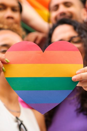 A group of LGBTQ people holding a rainbow heart celebrating International Pride Month.