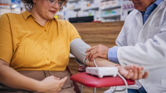 Male pharmacist measuring blood pressure to woman at the pharmacy.