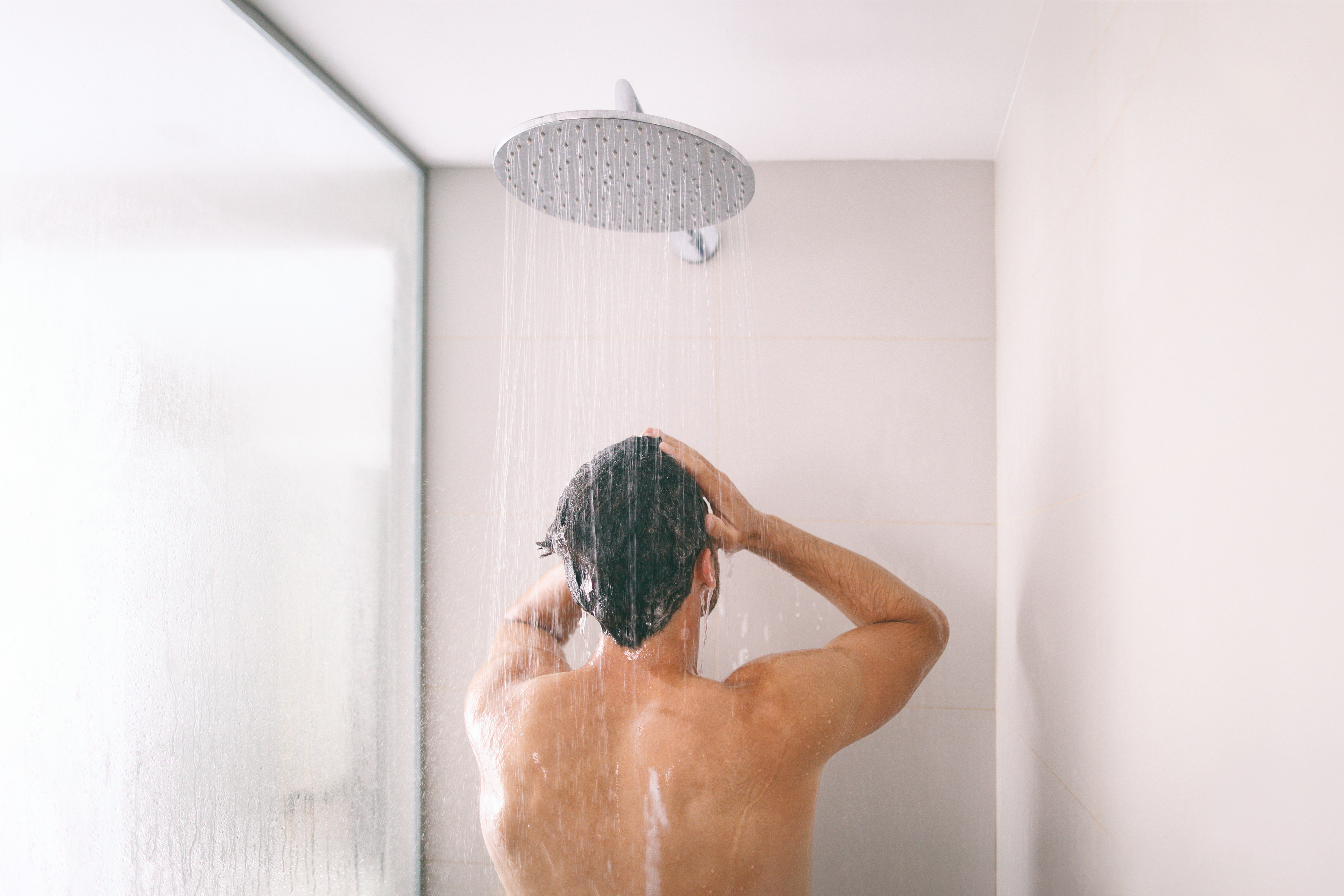 Man taking a shower washing hair with shampoo product under water falling from luxury rain shower head. Morning routine luxury hotel lifestyle guy showering. body care hygiene.