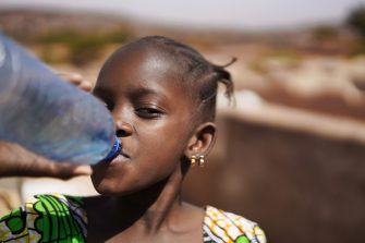 Close-up Of An African Girl With Earrings Drinking Water Straight From A Big Plastic Bottle 