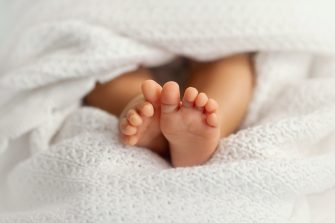 Adorable baby feet covered in a white blanket, maternity and babyhood concept - Image
