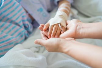 Little girl was sick and her hand was hold by her mother in hospital room. Selective focus,