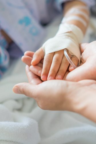 Little girl was sick and her hand was hold by her mother in hospital room. Selective focus,