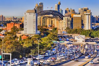 Rush hour traffic gridlock on busy Sydney main road.  Looking between two lanes of stationary vehicles with brake lights illuminated plus both red and green traffic lights.  A public transport bus is in the distance.  Horizontal, heat haze (shimmer).