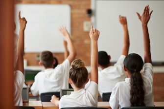 A young teacher at the front of the classroom listening to students.
