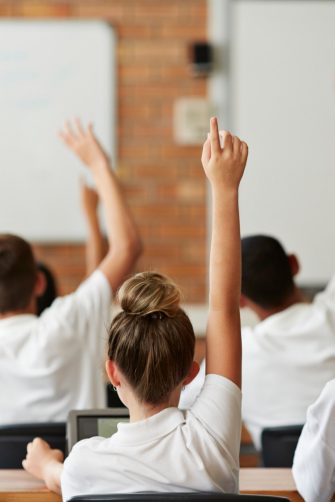 A young teacher at the front of the classroom listening to students.