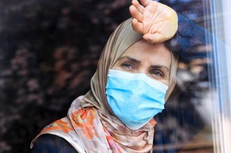 Woman in face mask and headscarf looking out of window