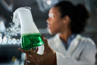 Close up of African American female chemist holding beaker with chemical reaction in laboratory.