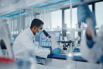 Indian male scientist looking under microscope in lab