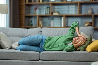 An elderly woman is lying on the sofa at home and suffers from a headache, pressure, tension. holding his head Stress, got sick.