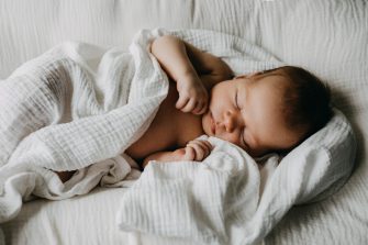 Newborn baby sleeping in a baby nest, covered with white muslin blanket.
