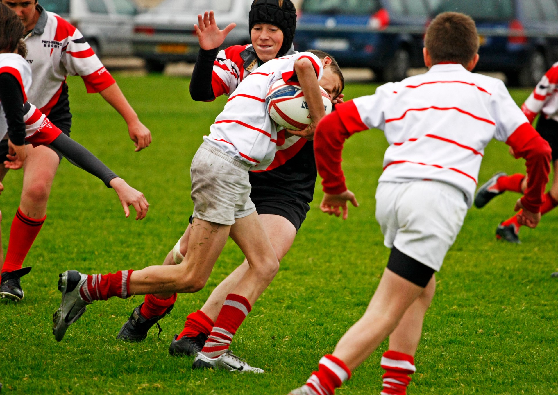 An action of shot of young boys playing rugby. One boy is leaning into a tackle with the ball tucked under his arm.