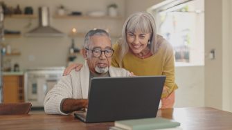 Senior couple, home and laptop for internet research with  for retirement and social media update. Interracial marriage, old man and woman with computer in kitchen for video call app and virtual chat