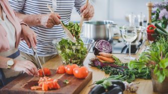 Close-up of senior people cutting tomatoes and mixing salad while preparing healthy dinner