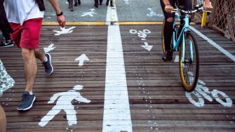 Pedestrian and bicycle riders sharing the street lanes with road marking in the city. People walking and riding on bicycle on city street.