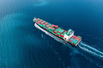 A cargo ship loaded with green and yellow containers makes its may across a vast ocean.