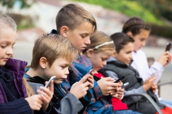 Outdoor portrait of little girls and boys playing with phones 