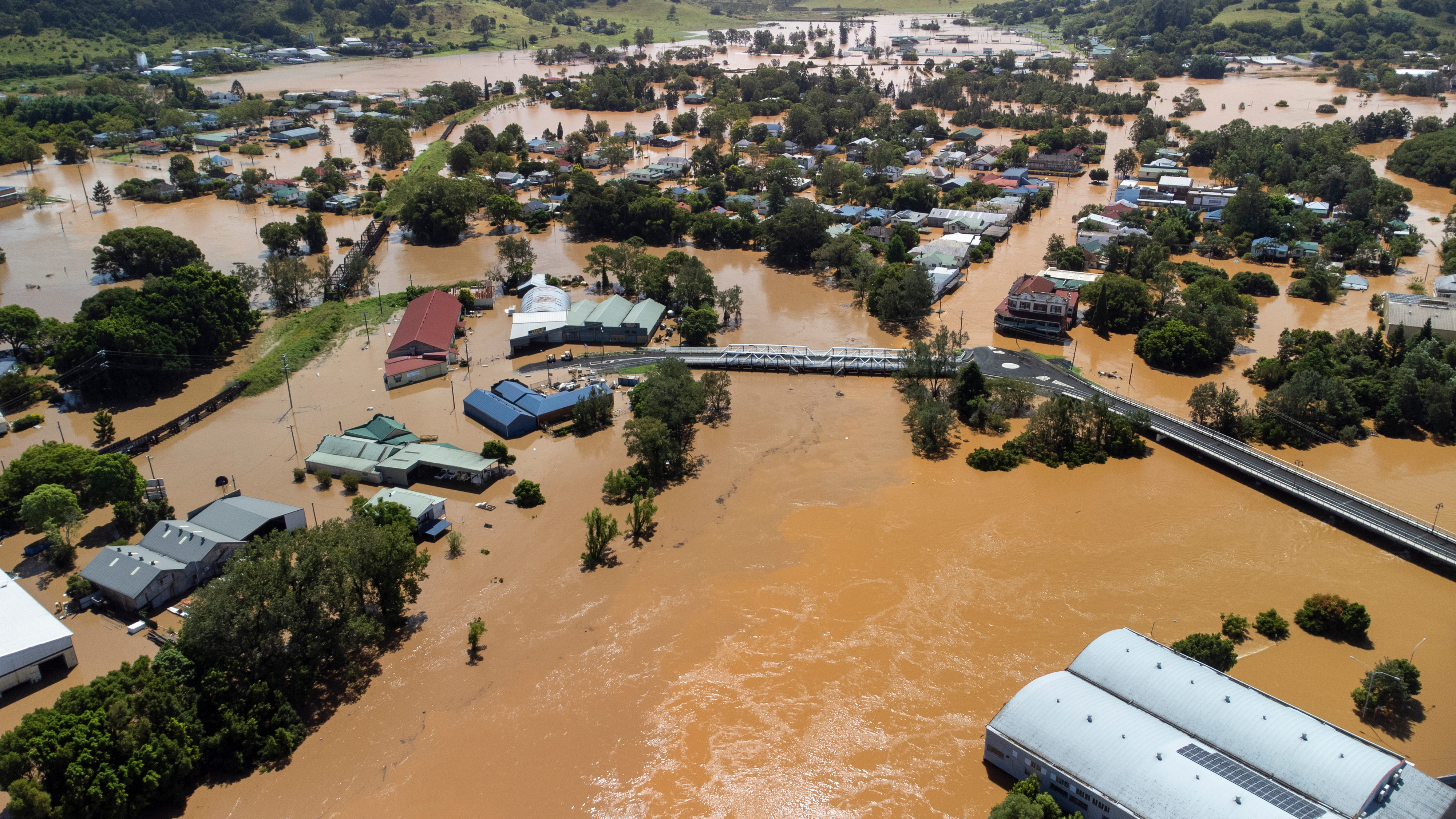 Brown flood water covers roads and engulfs houses and trees.