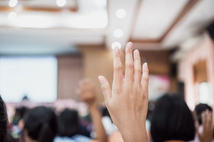 Audience or students raising hands up at conference to answer question while speaker speech at seminar hall with crowd groups, arms of large group in classroom for vote or questions
