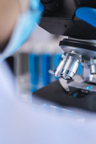 Scientist analyzing microscope slide at laboratory. Young woman technician is examining a histological sample, a biopsy in the laboratory of cancer research