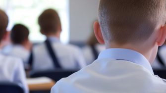 Students in uniform seated at desks in a classroom, attentively listening to the teacher