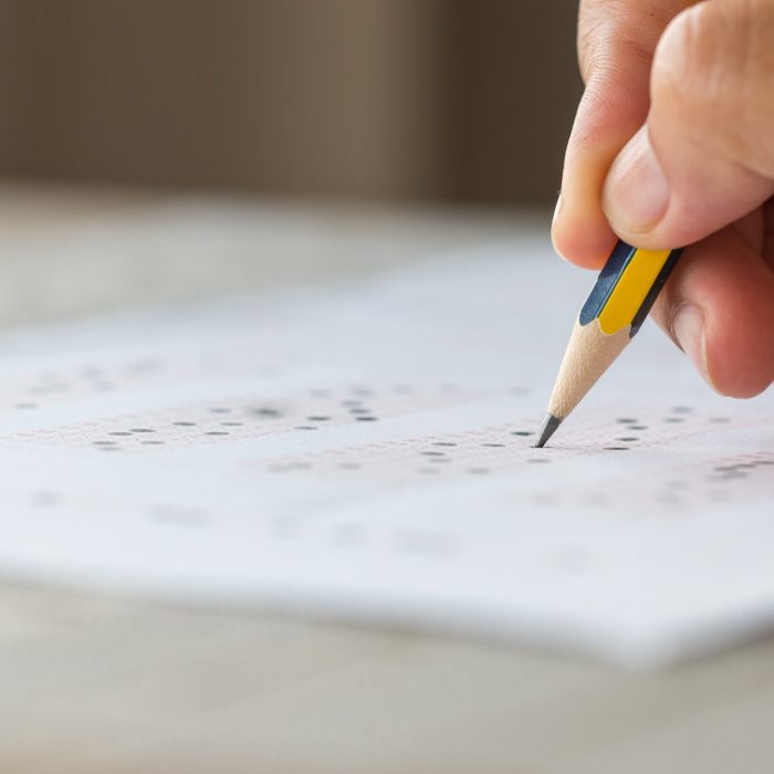 Close-up of a hand using a pencil to fill in answers on a multiple-choice test sheet.