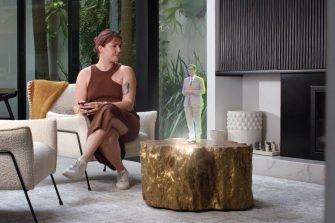 A women sat on a sofa watching a holographic weather report