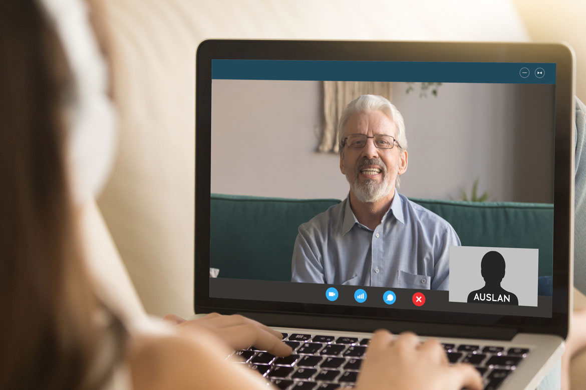 Image of a person using a laptop with one person in the main view of screen. To the bottom right of screen is a small image of a Auslan Interpreter.