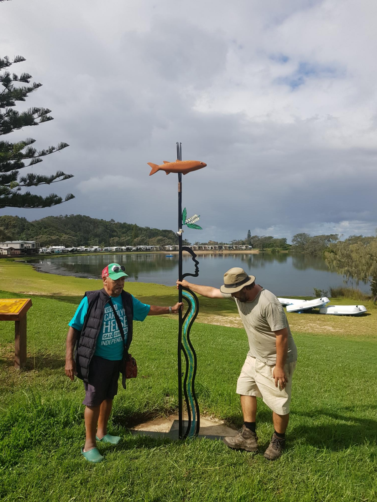 Artist and one other person standing next to sculpture located in public space with body of water in the background