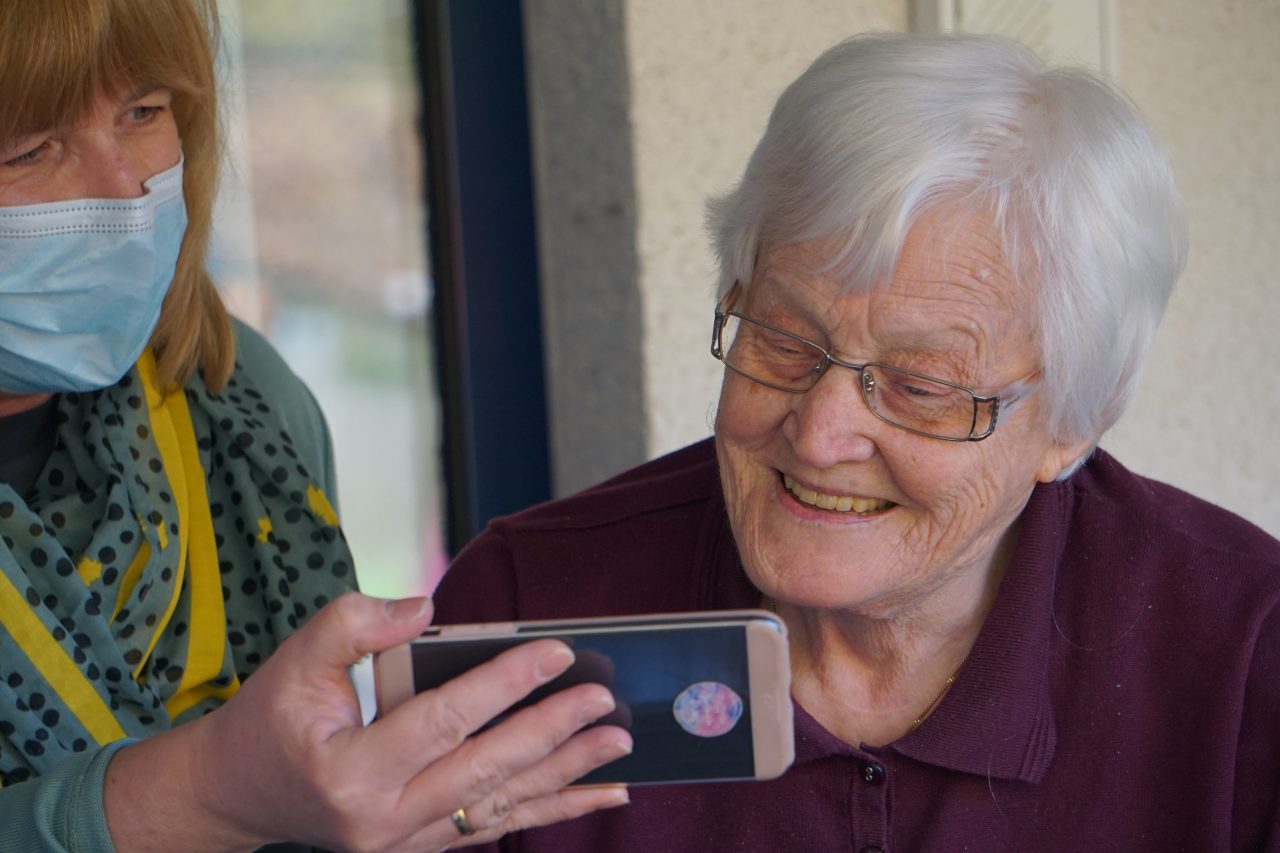 Elderly woman looking at mobile phone screen being held by a person 
