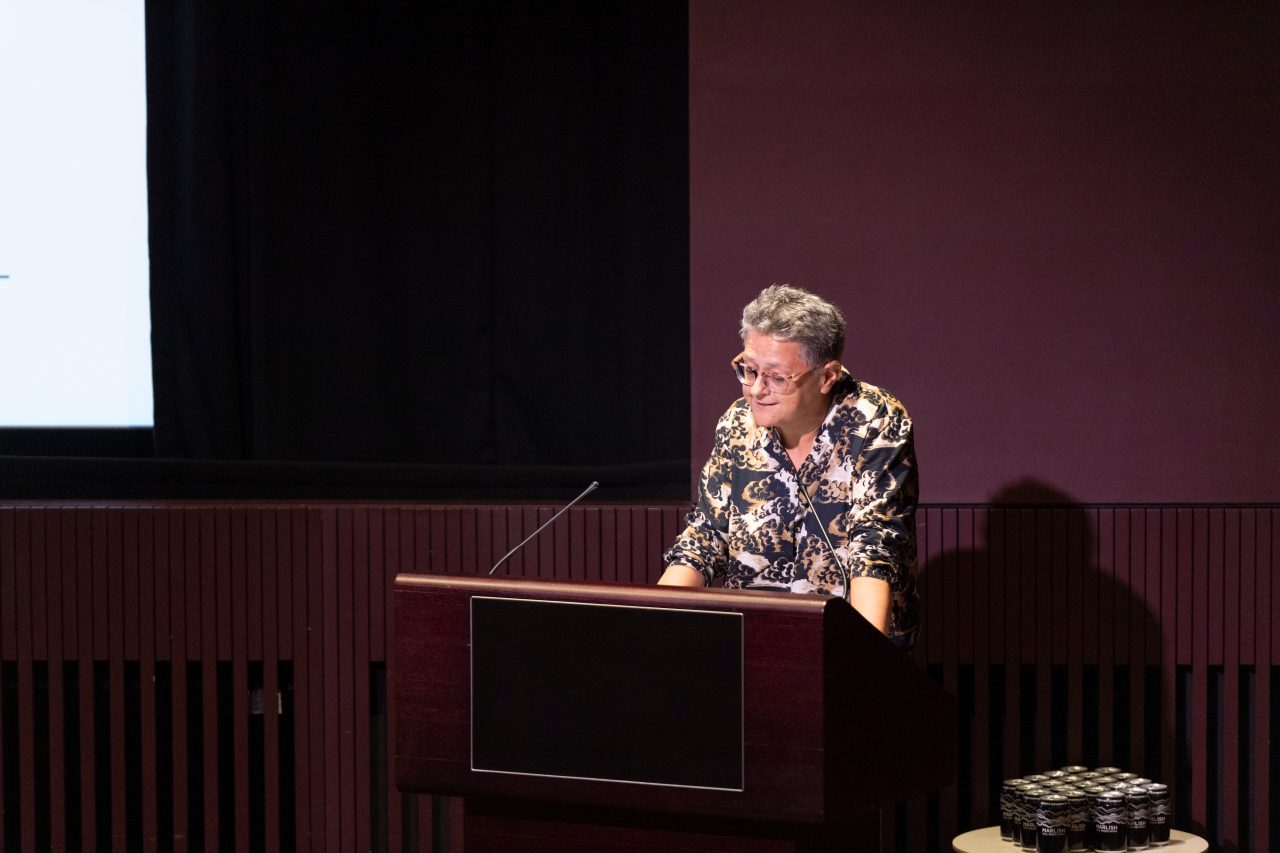A person in a colourful shirt speaks at a lectern