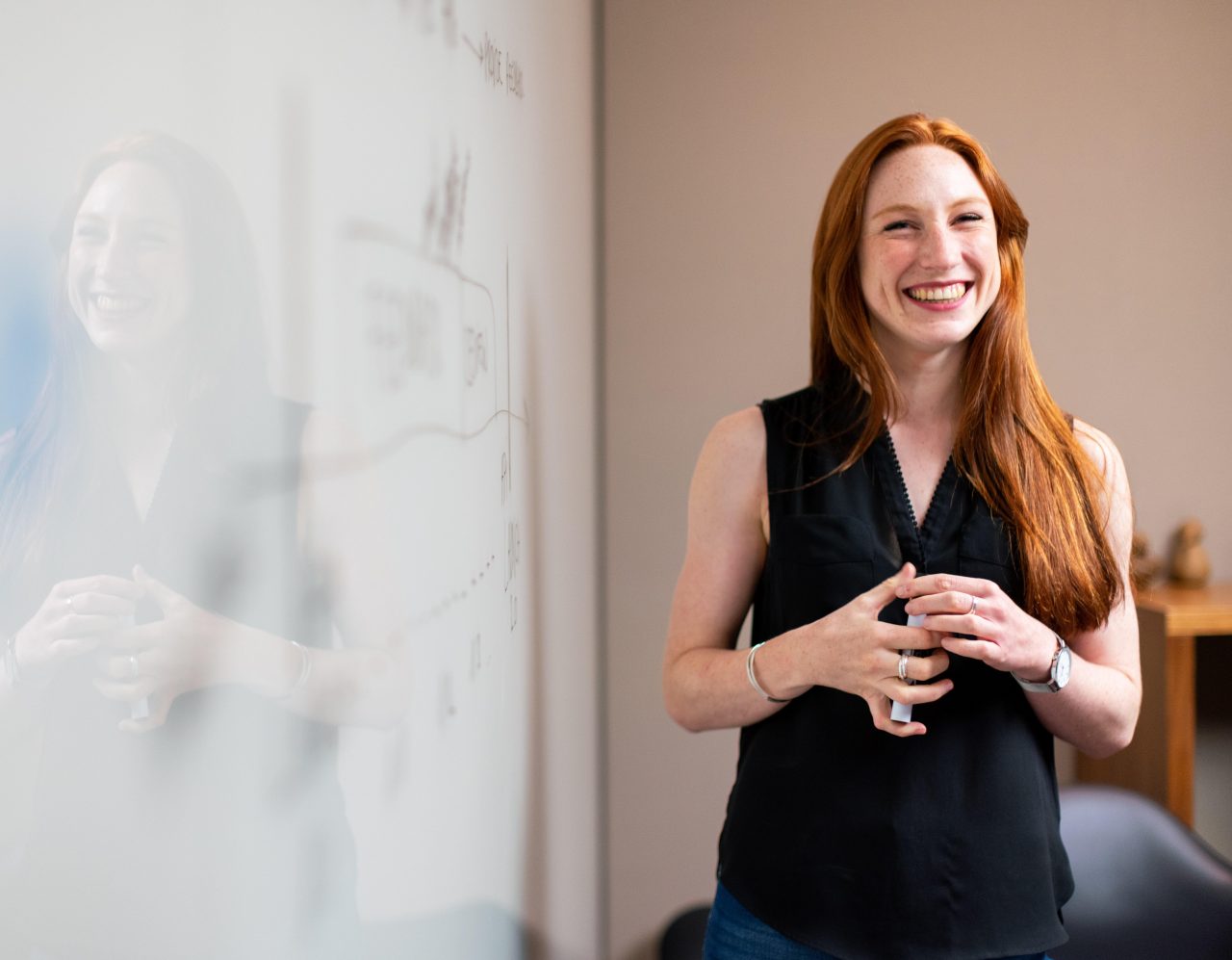 Woman with red hair and black top standing at a whiteboard