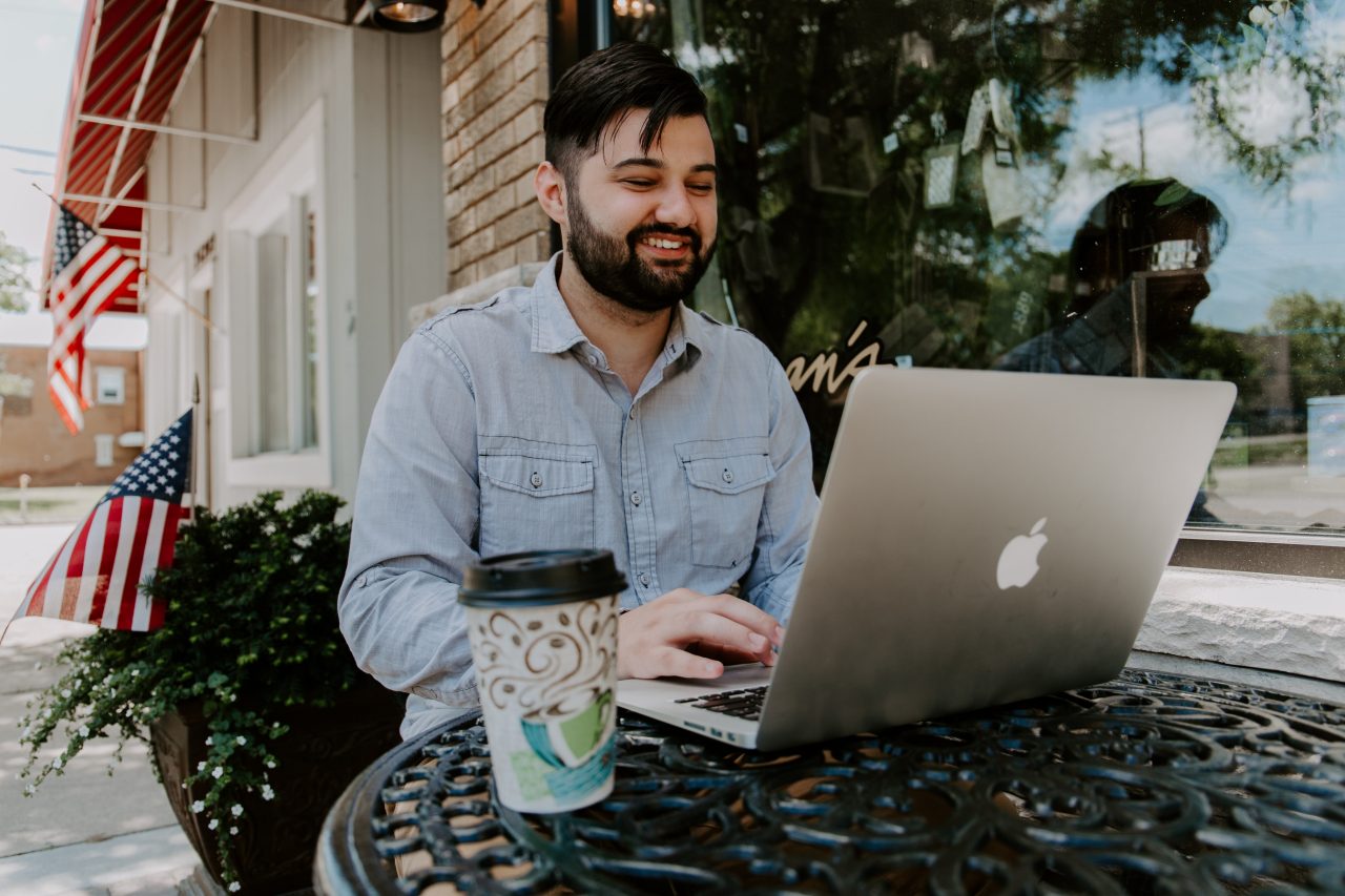 Man in gray demin dress shirt smiling while using Macbook 