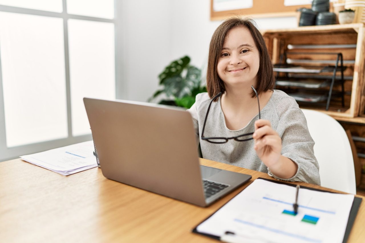 Brunette woman with down syndrome working using laptop at business office