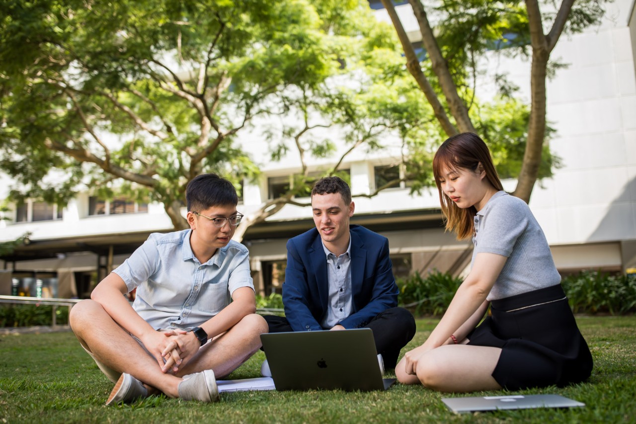 three students studying from a laptop on campus
