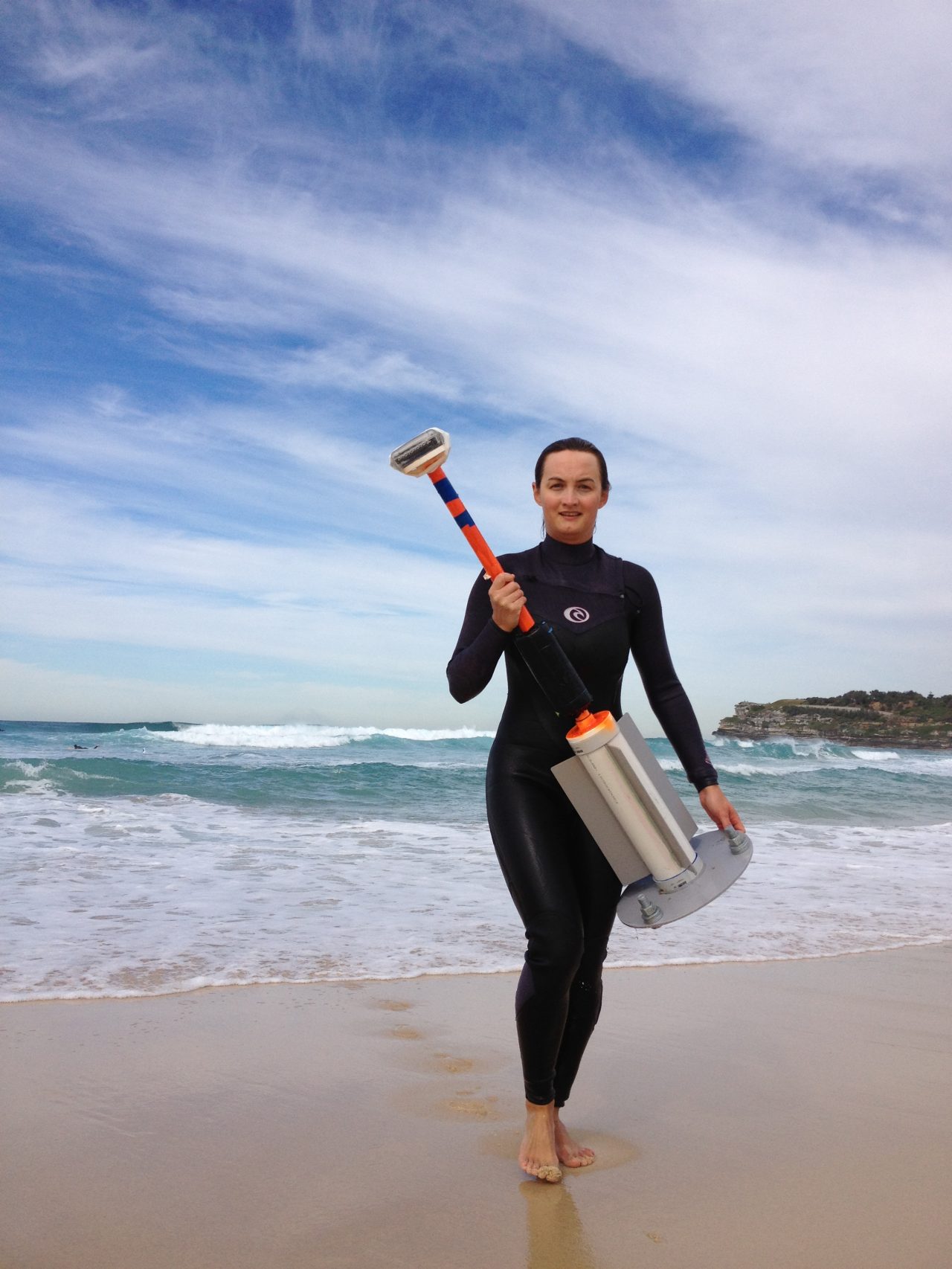 Kristen on the beach in a wetsuit holding a vaccum device 