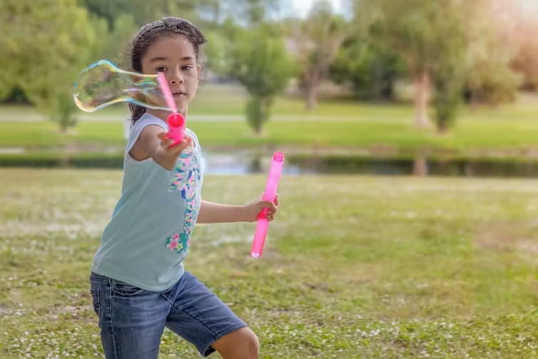 A young girl playing outdoors with a bubble blower