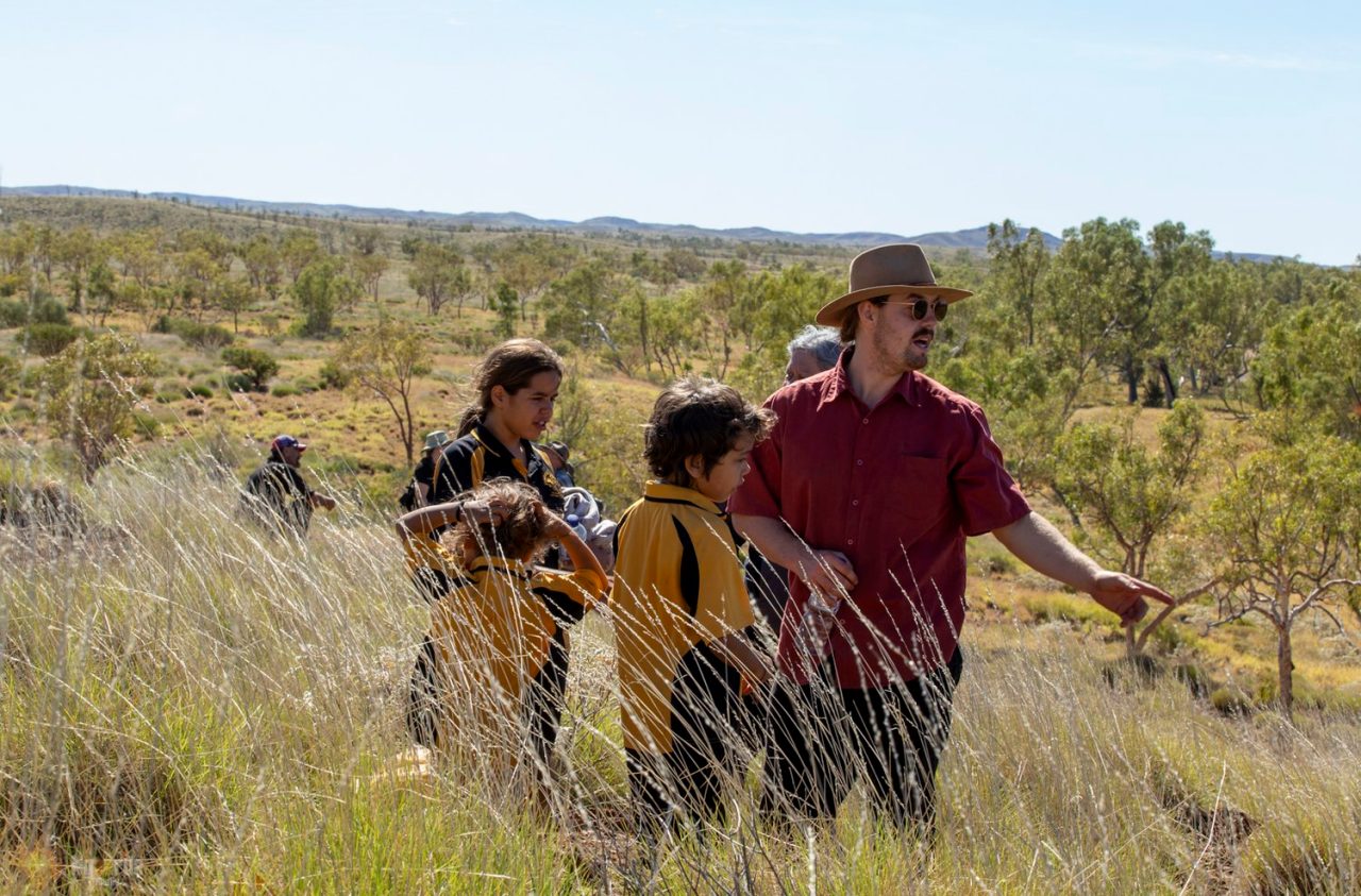 A man is pointing at rock formations to school children in the Pilbara