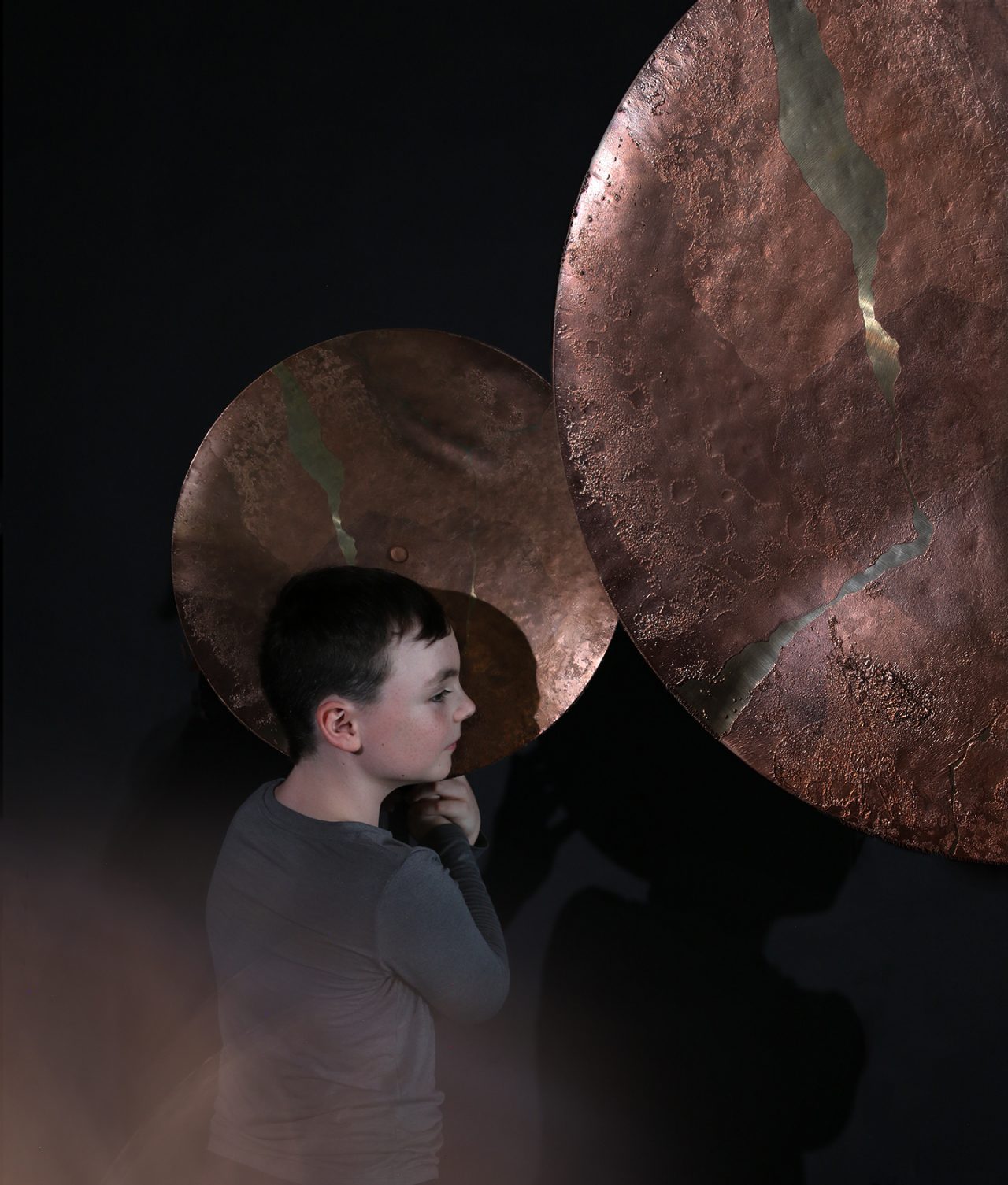A boy listens to sounds through a brass sculpture