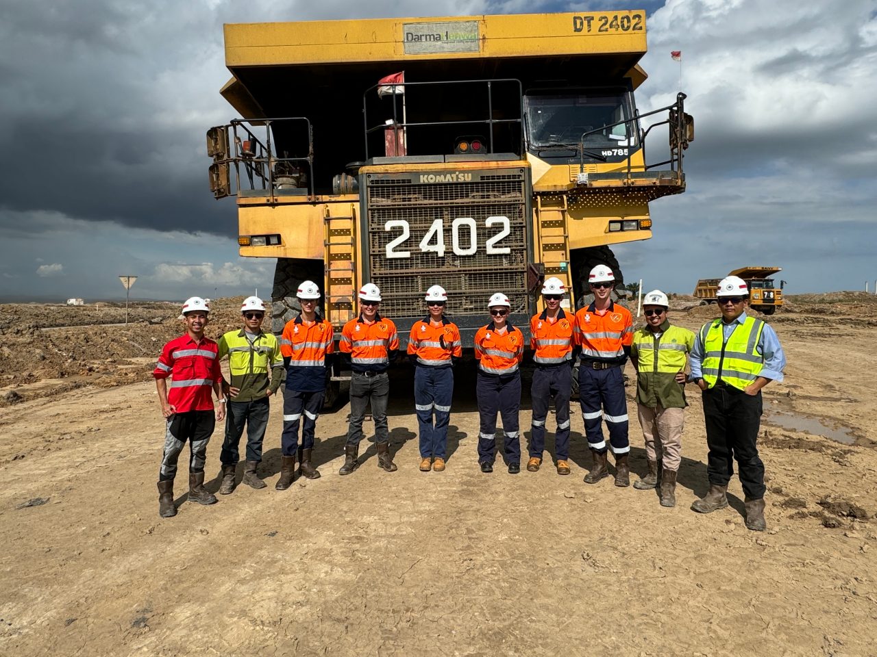 A group of people in hihg-vis clothing standing in front of a massive mining truck.