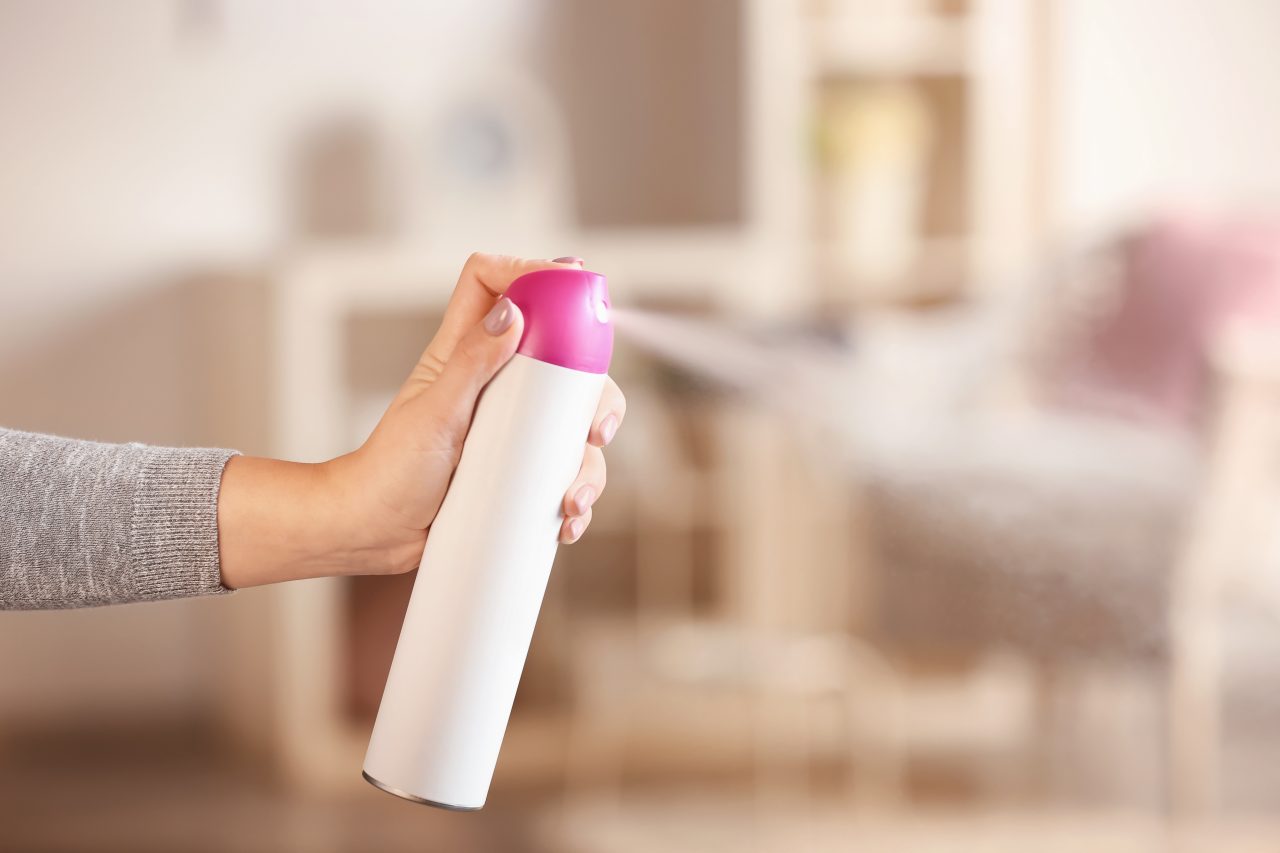A hand spraying a bottle of air freshener in the home