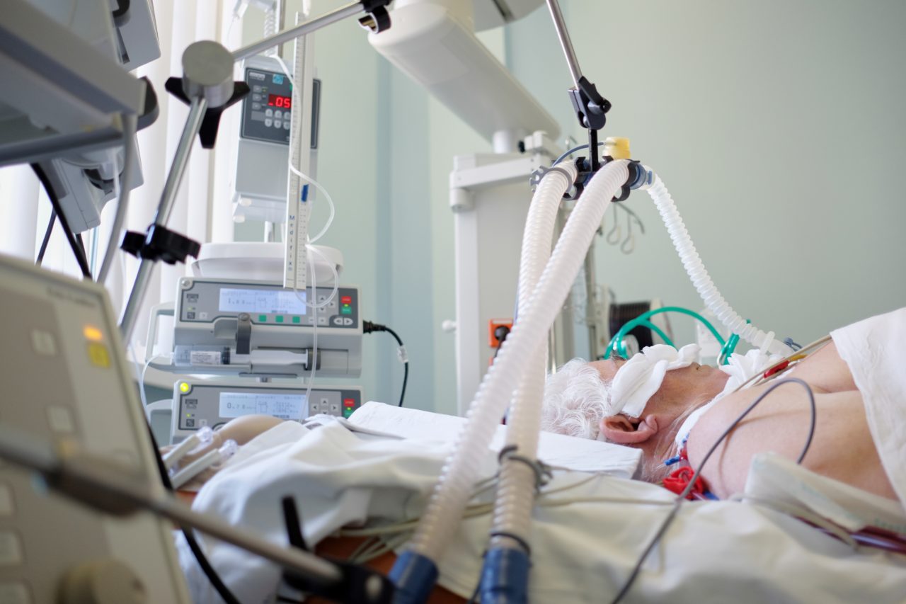 Intubated senior under ventilator lying in coma in intensive care department.